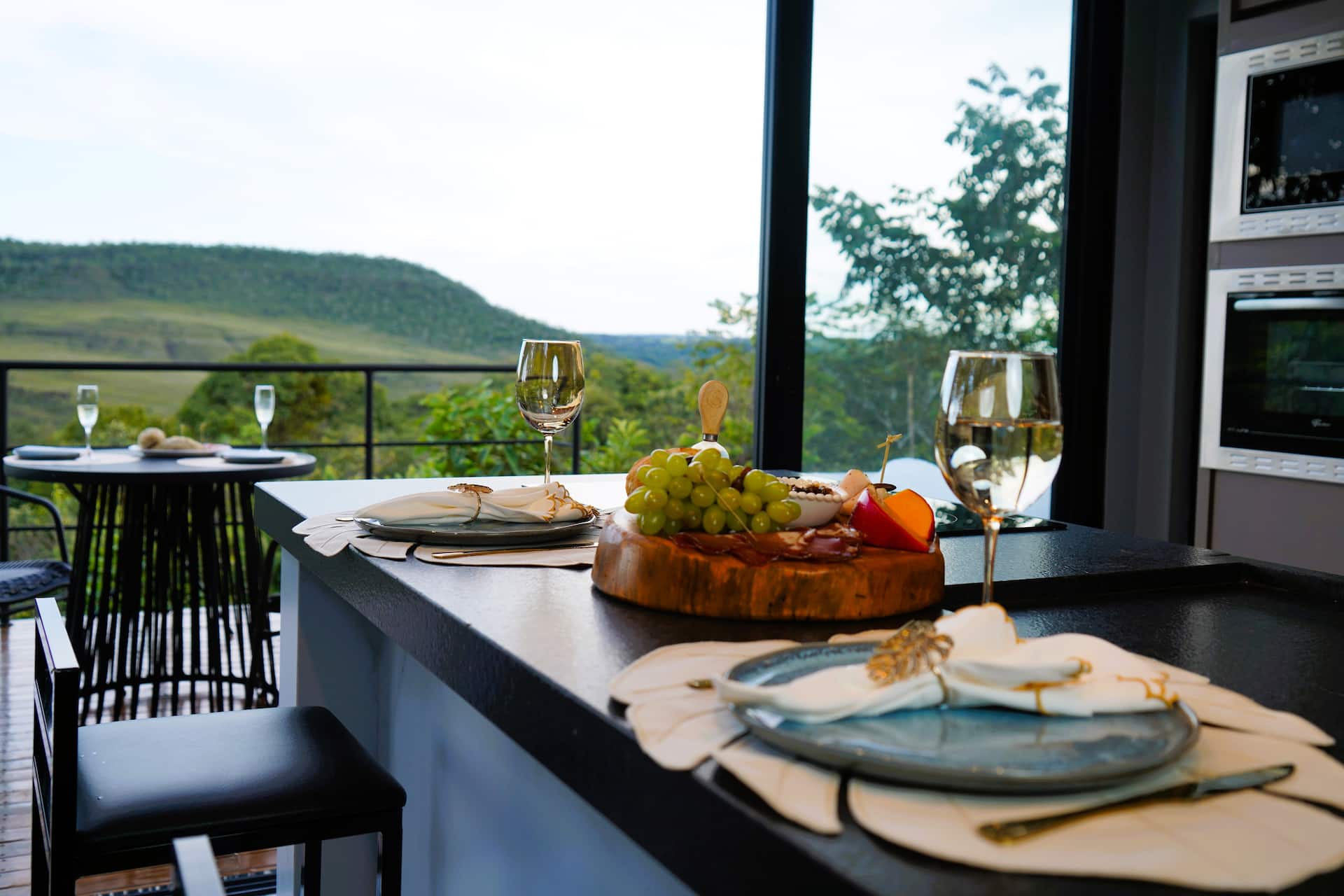 Taça de vinho e tábua de frios na bancada com vista para as colinas do cerrado
