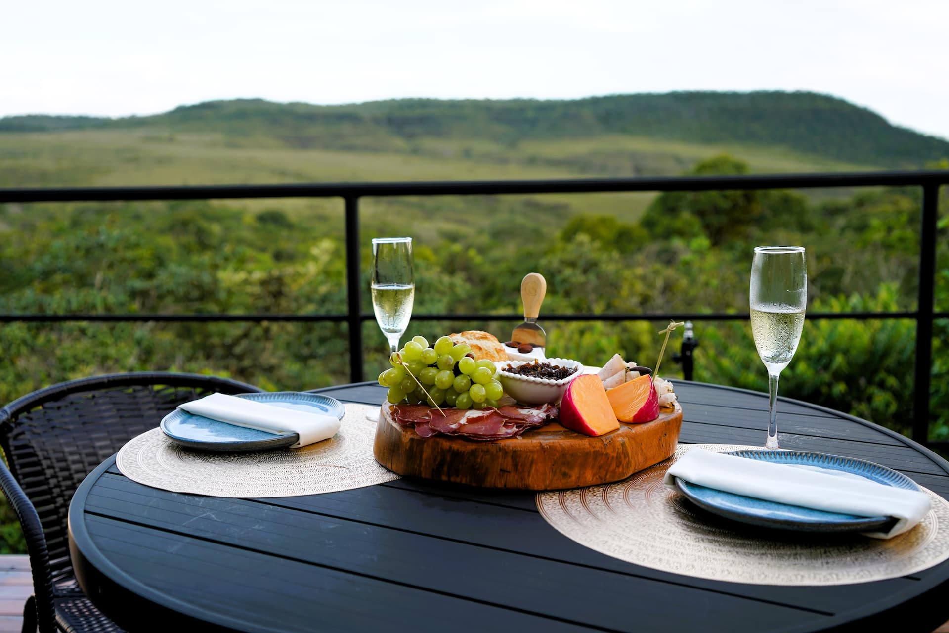 Taças de espumante e tábua de frios na mesa externa com a serra ao fundo