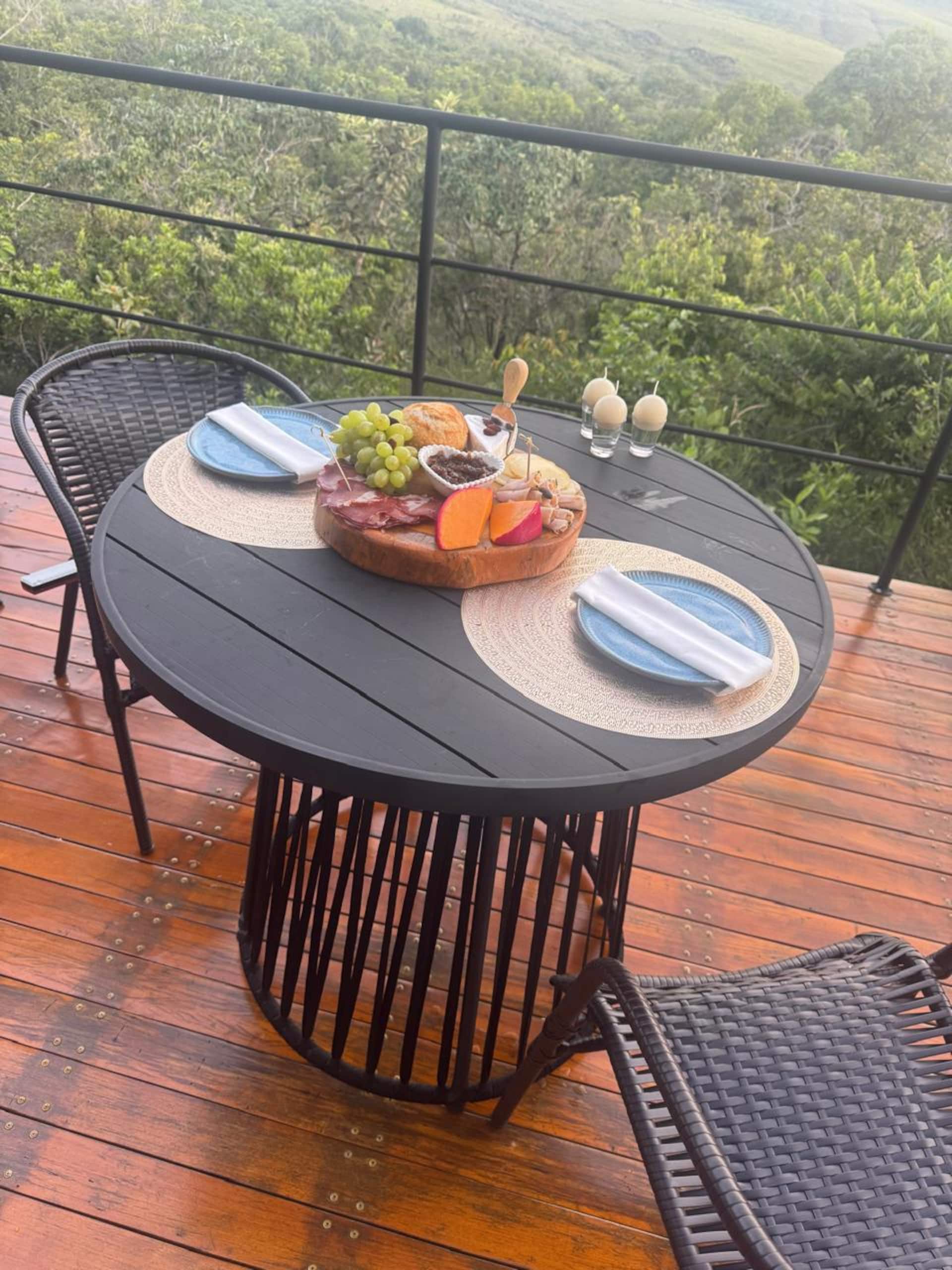 Mesa redonda no deck de madeira com tábua de frios e vista para a mata