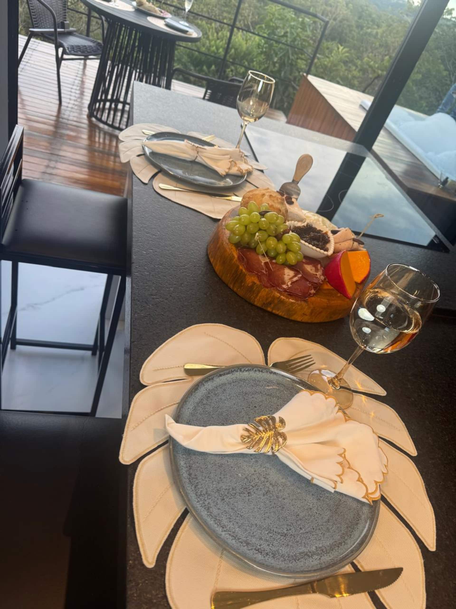 Mesa posta na varanda com taças de vinho, vidraça e piscina ao fundo