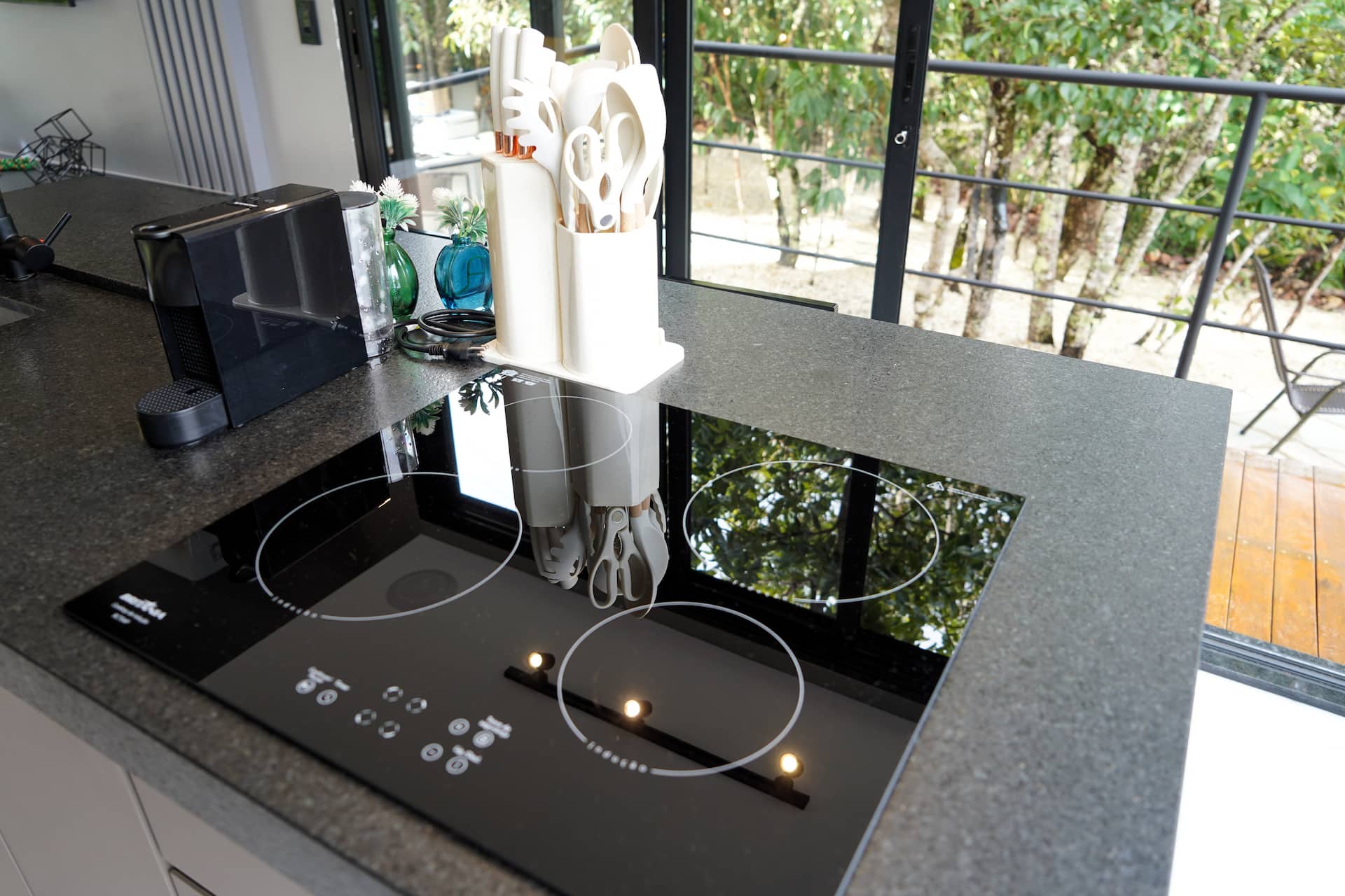 Cooktop de indução com utensílios sobre a bancada e a mata ao fundo pela janela