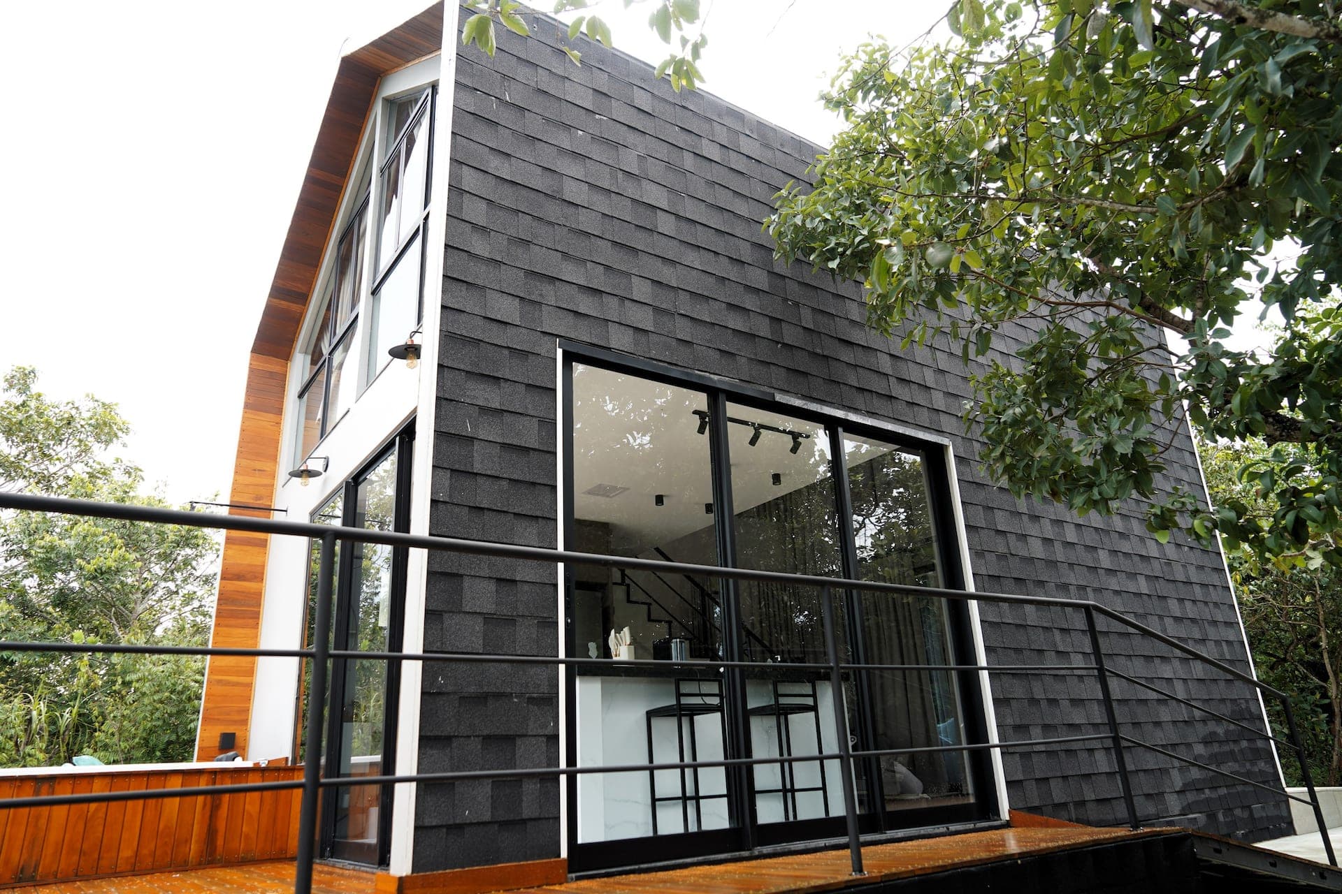 Fachada em telhas shingle grafite com empena de vidro e deck de madeira ipê