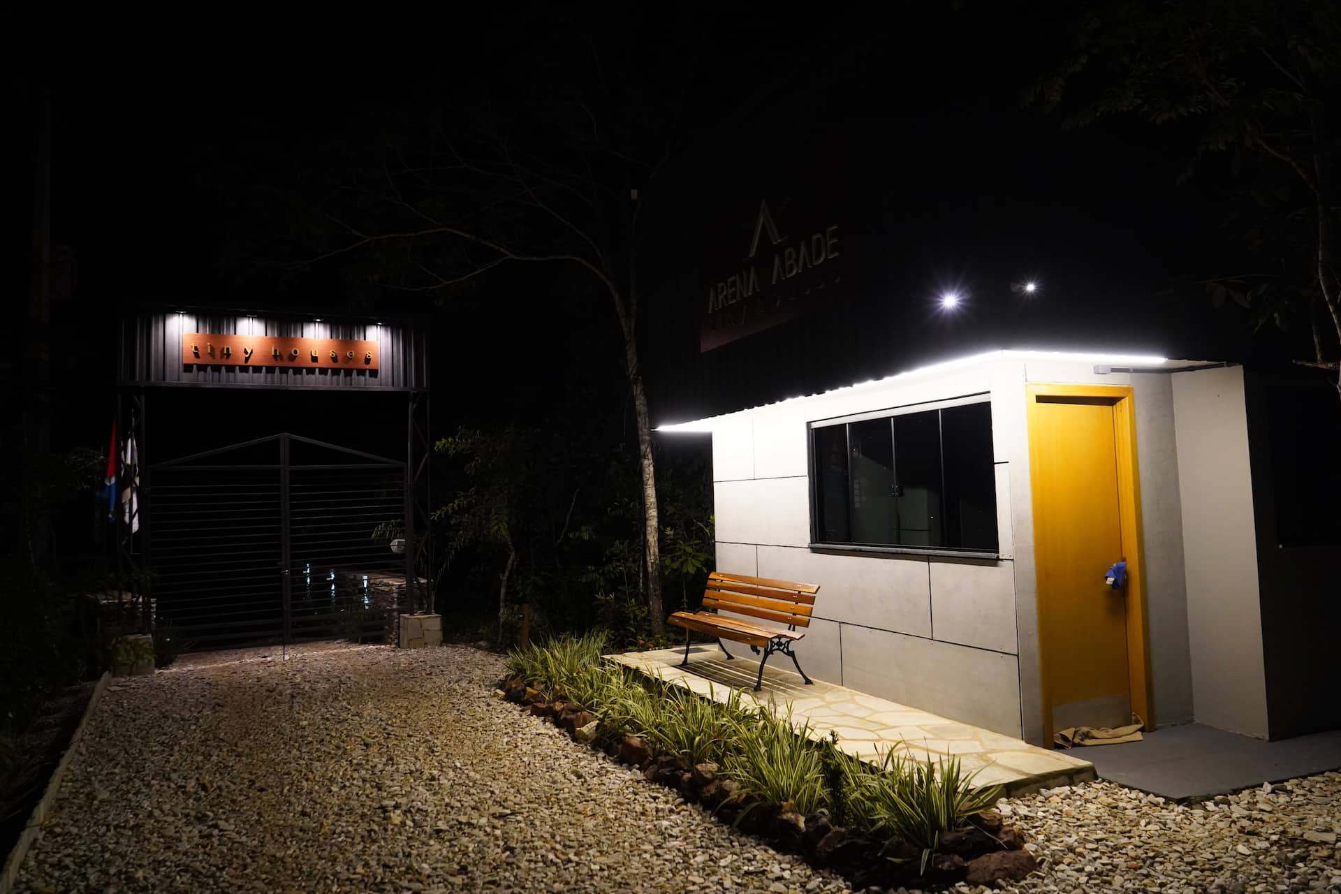 Recepção à noite com porta amarela iluminada e banco de madeira na entrada
