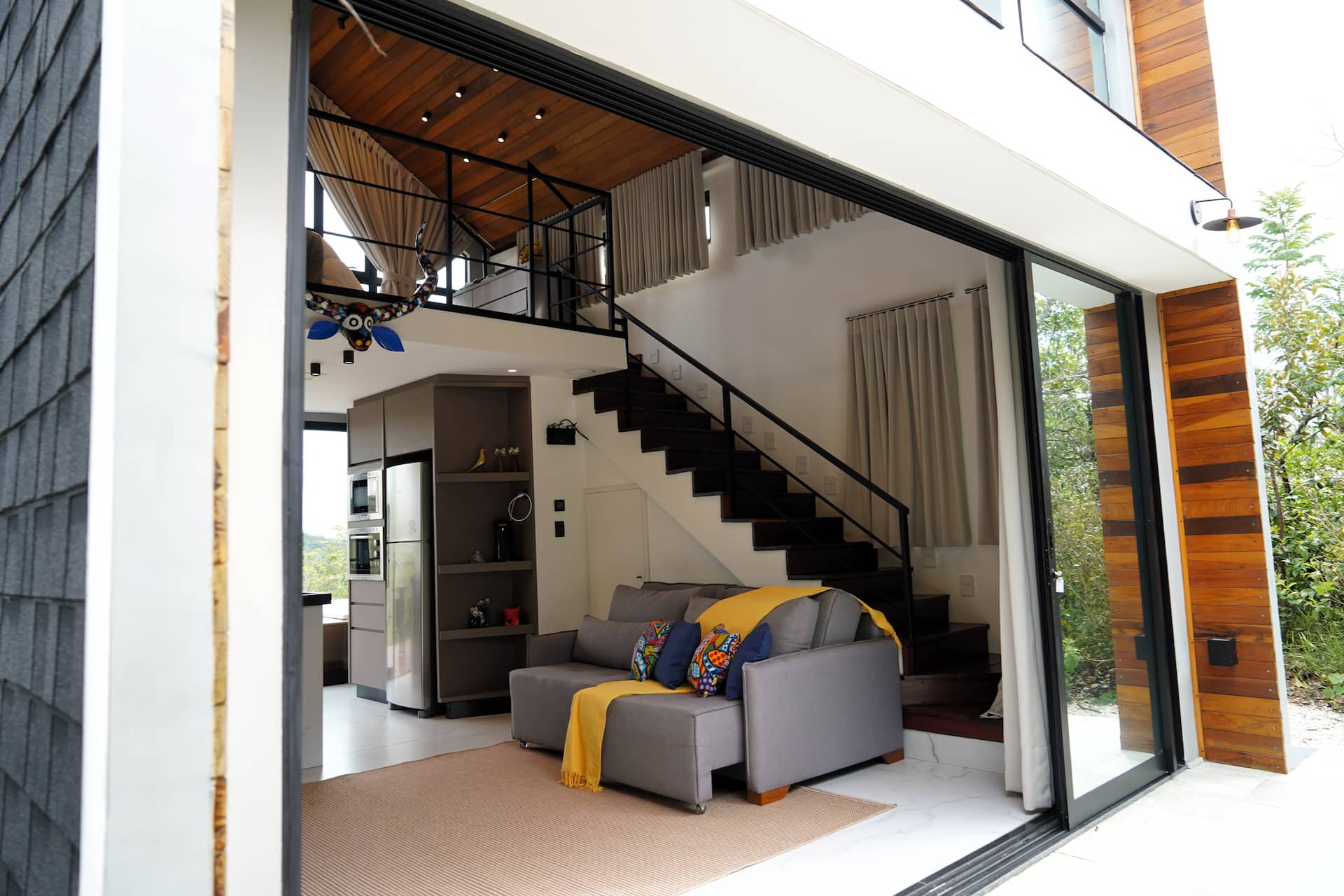 Vista da varanda para o interior da sala, com mezanino e escada aparentes