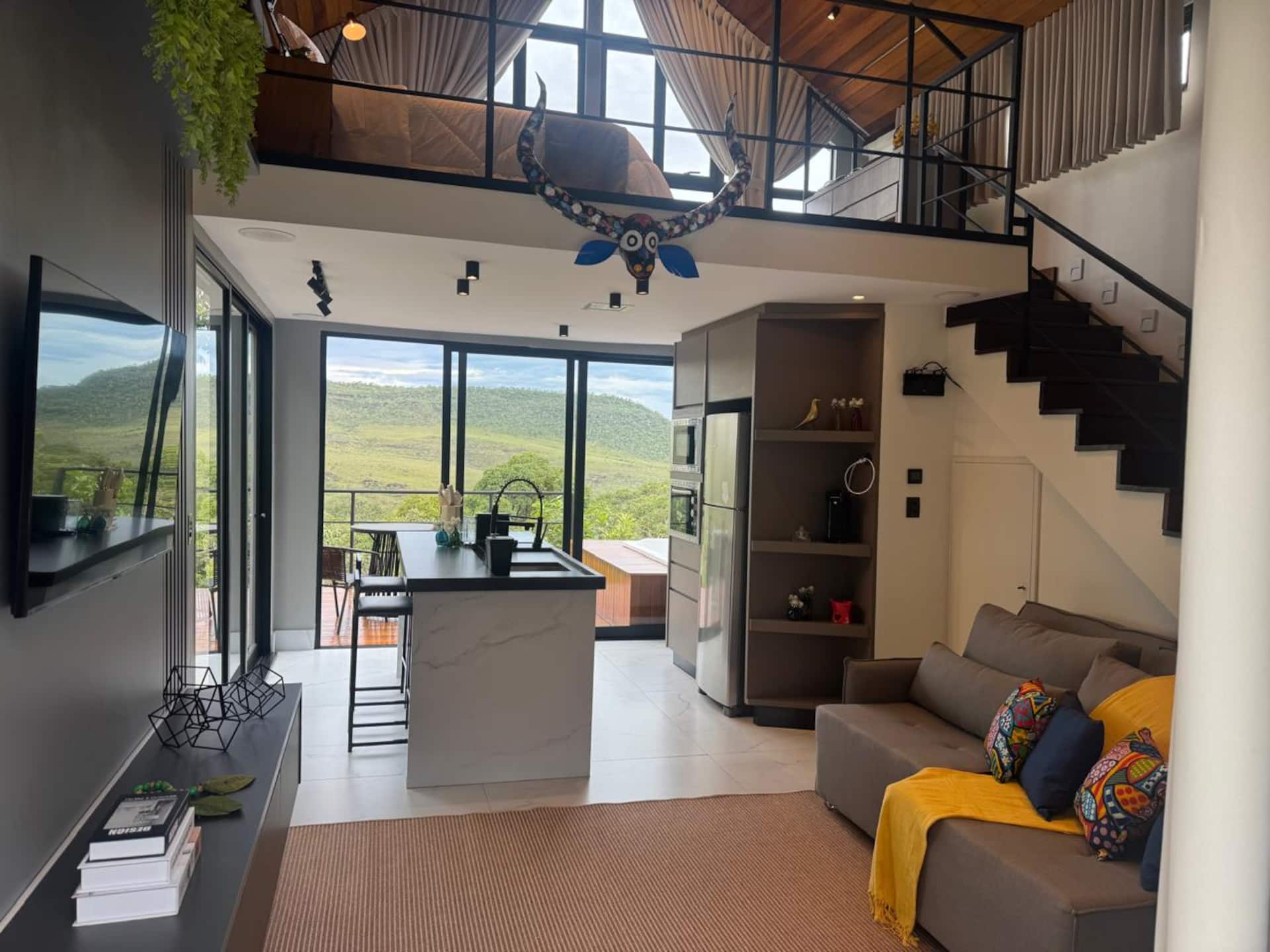 Sala integrada à cozinha, com mezanino, escada e vista para a serra