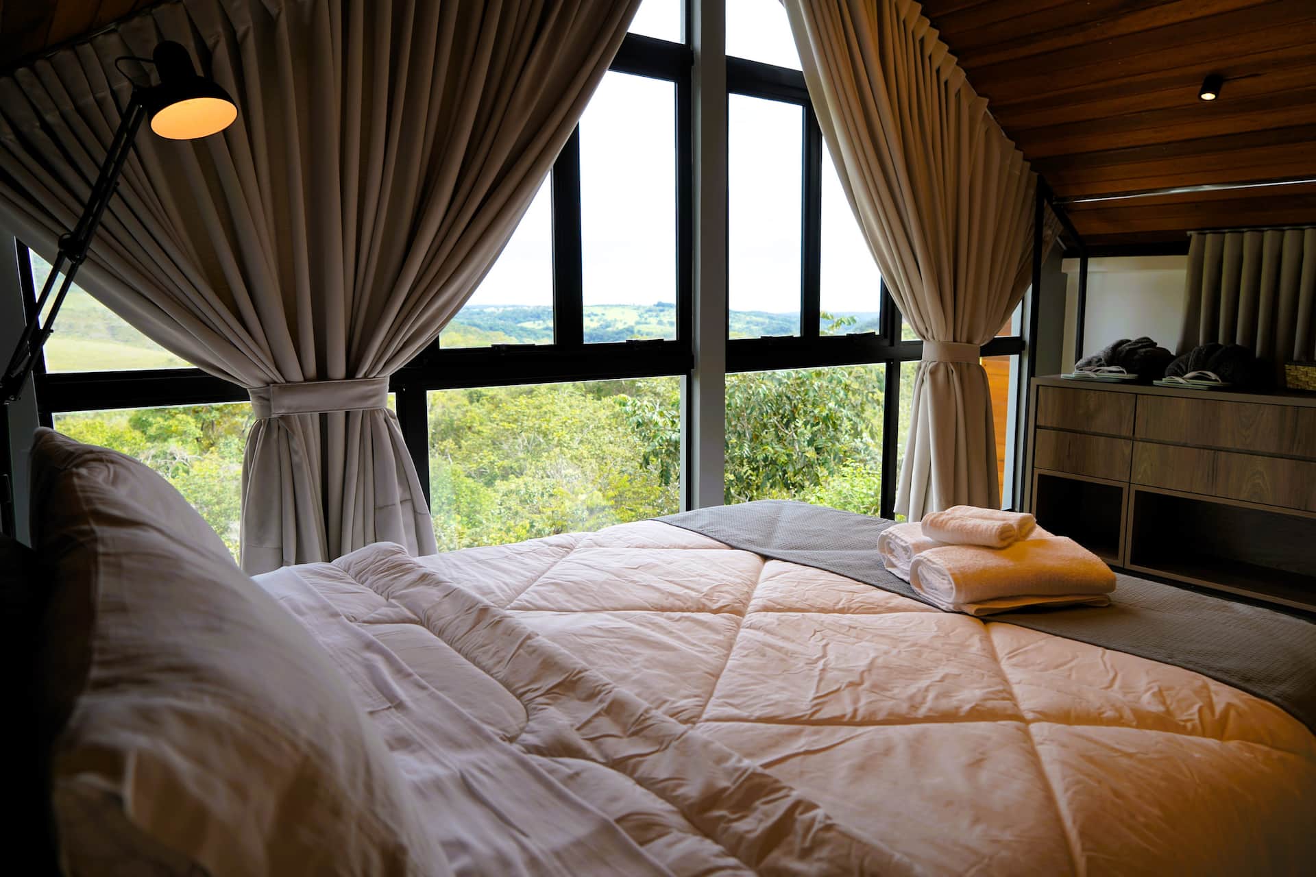 Cama junto à vidraça com cortinas blackout abertas e vista para o vale