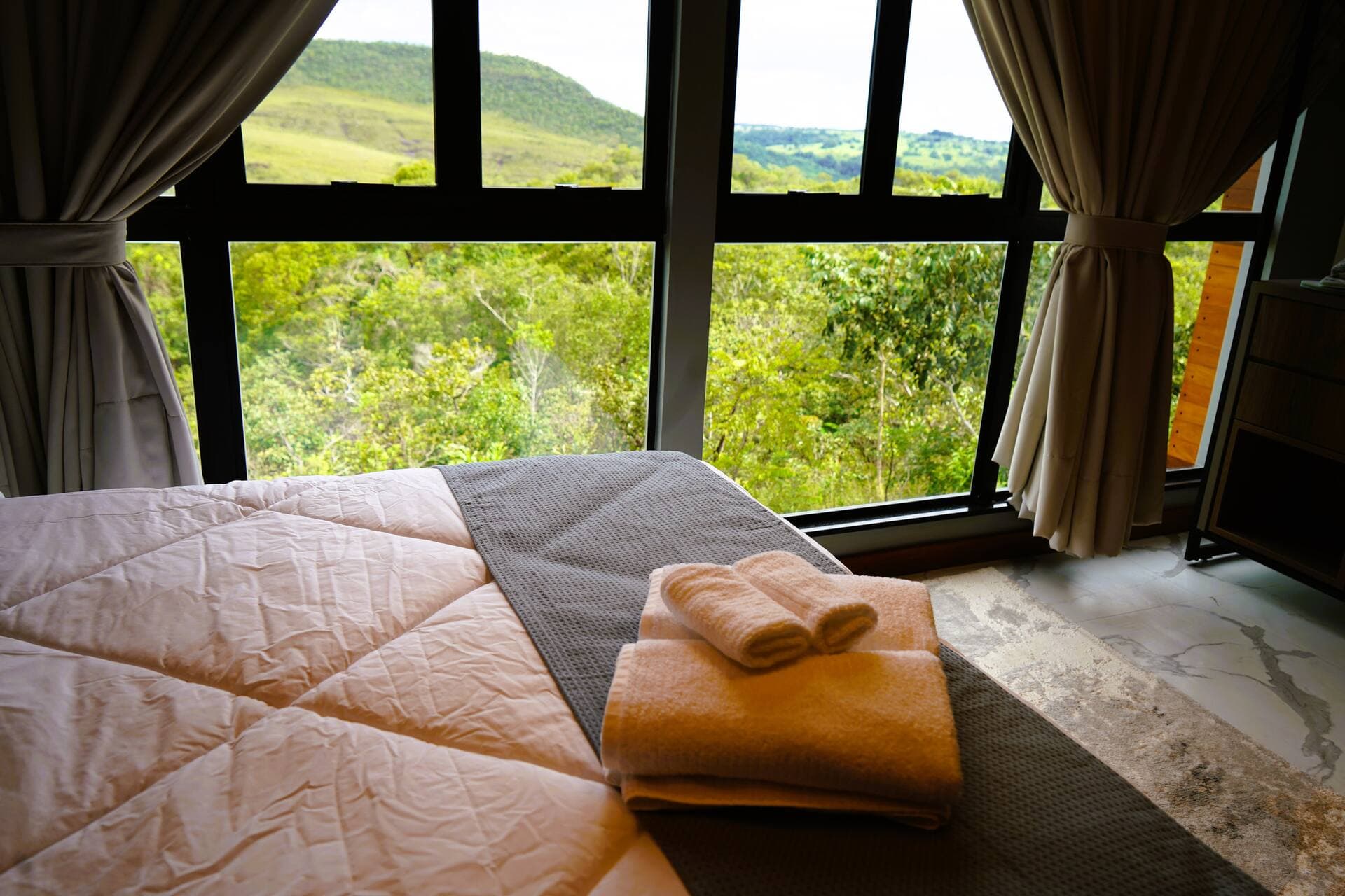 Toalhas dobradas sobre a cama com vista para as colinas pela janela