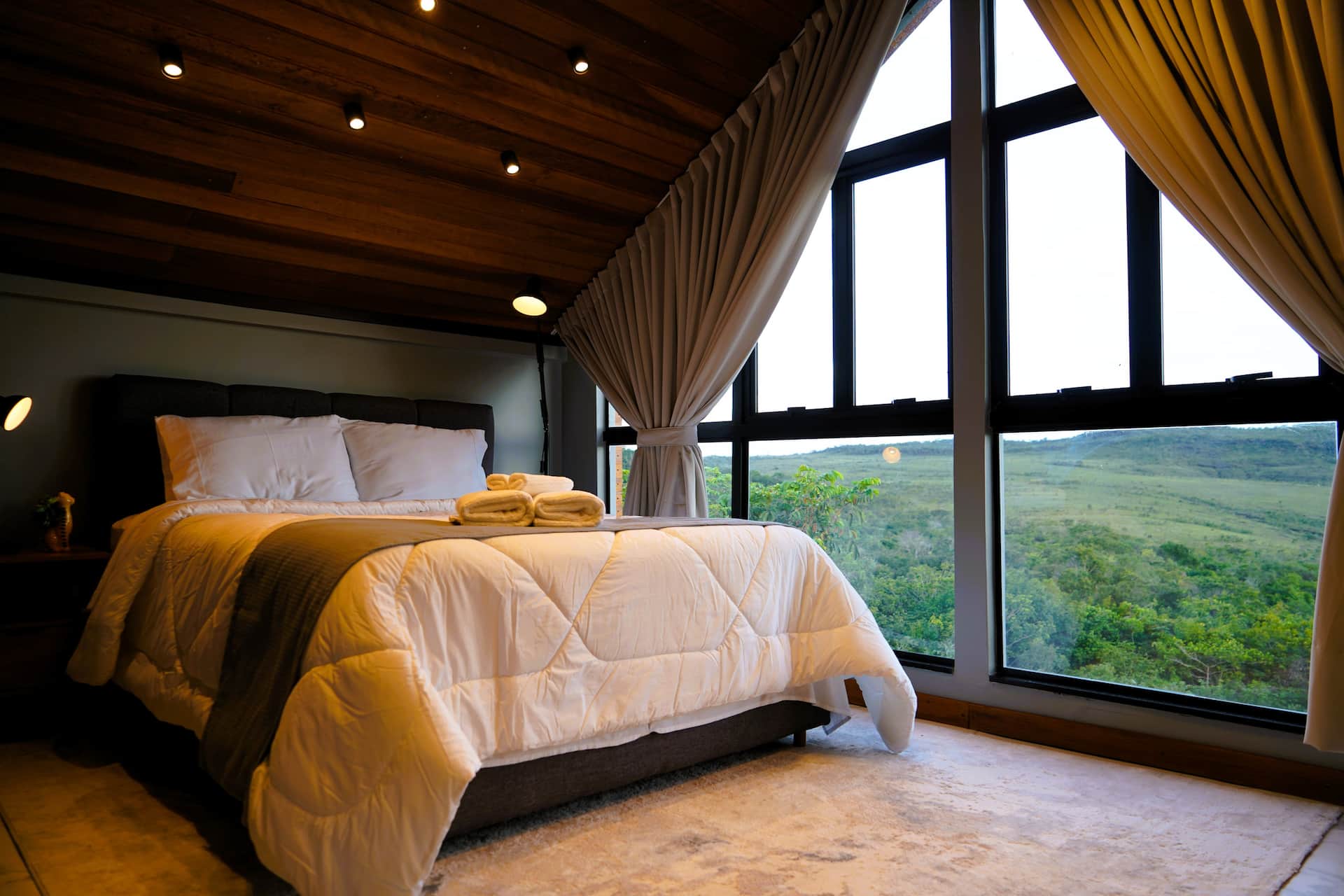 Cama de casal com cortinas blackout e vista para o horizonte do cerrado ao entardecer